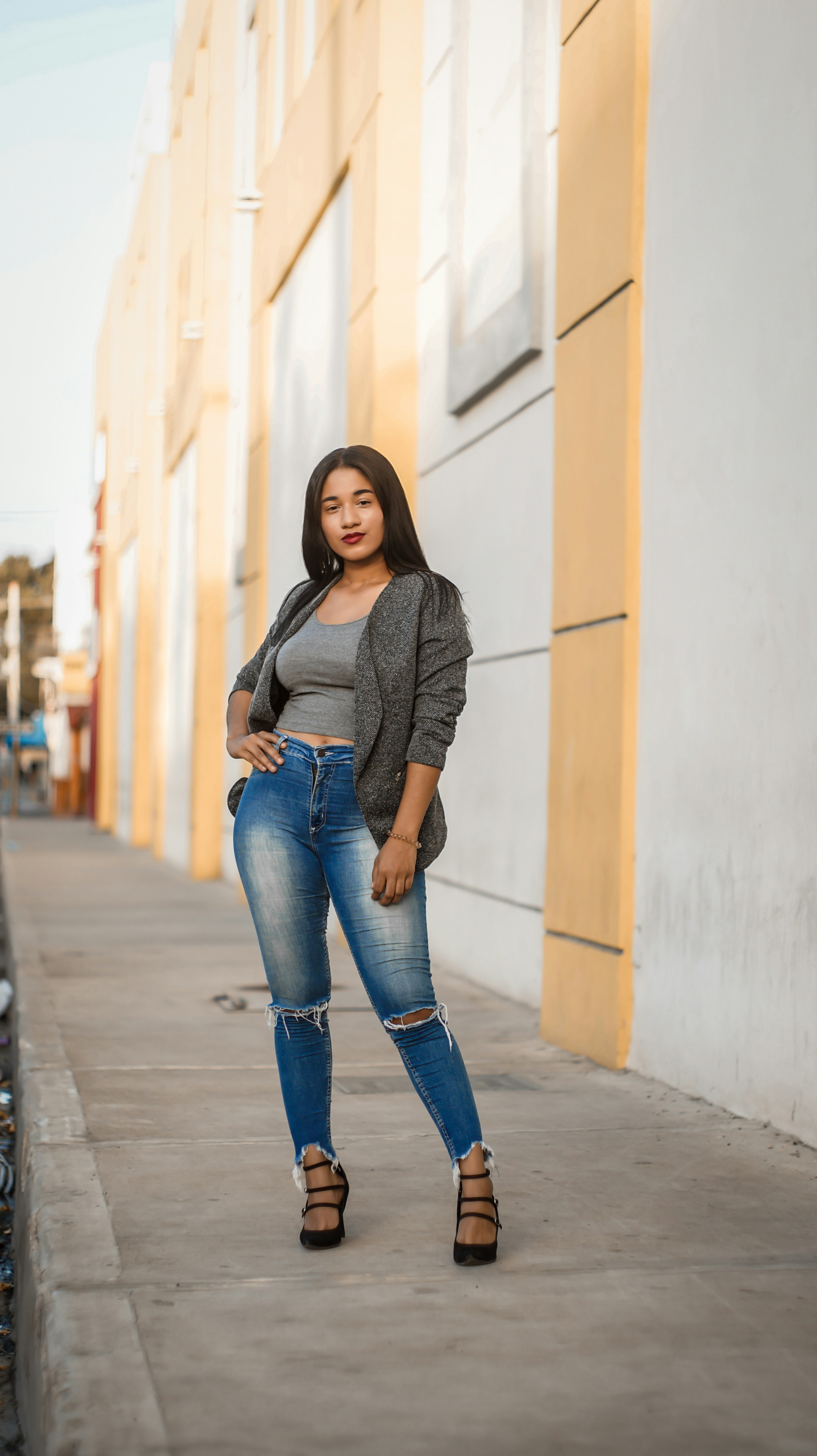 woman in gray long sleeve shirt and blue denim jeans standing on sidewalk during daytime